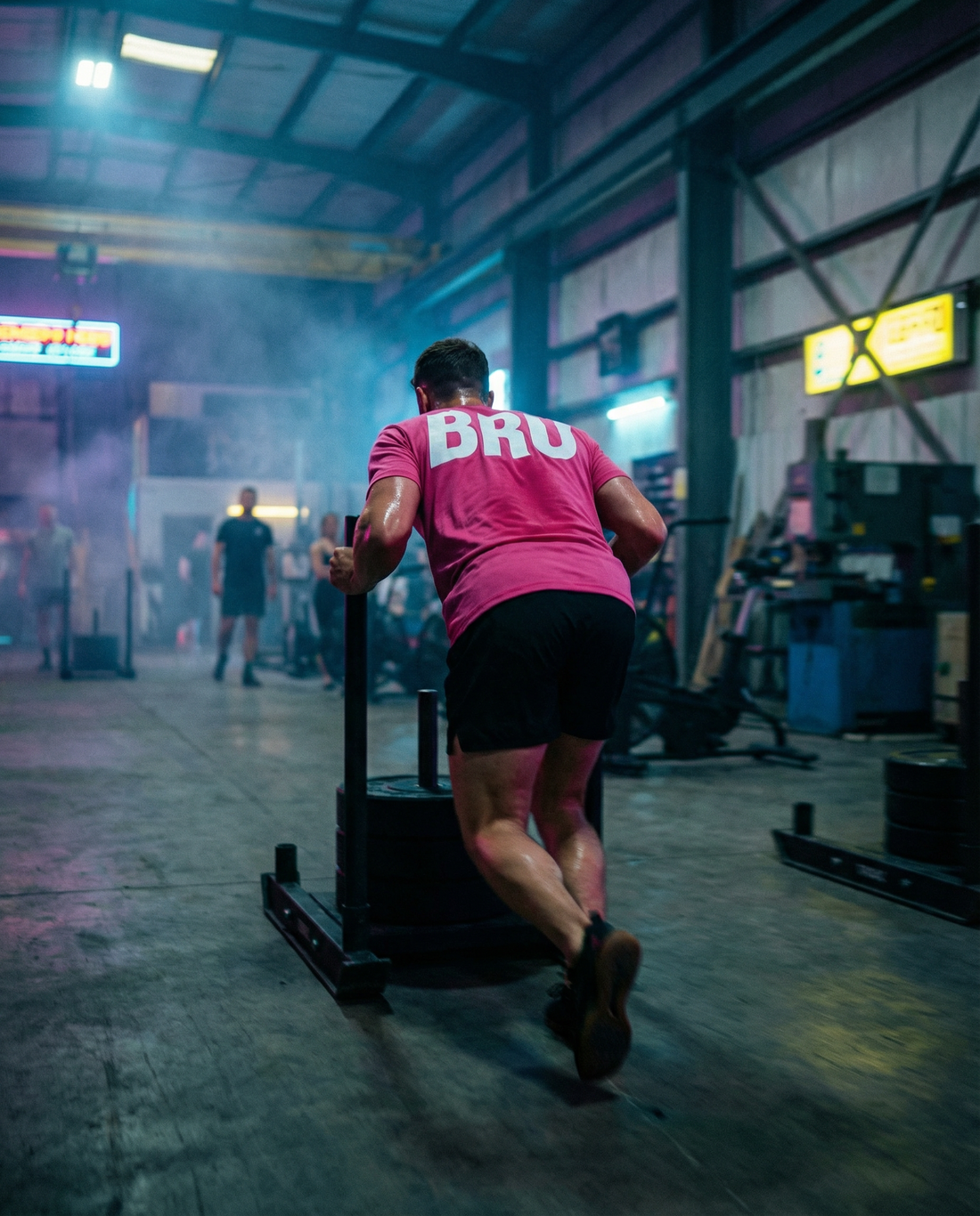Athlète qui pousse un sled en t-shirt rose et short noir BRO, entraînement Hyrox